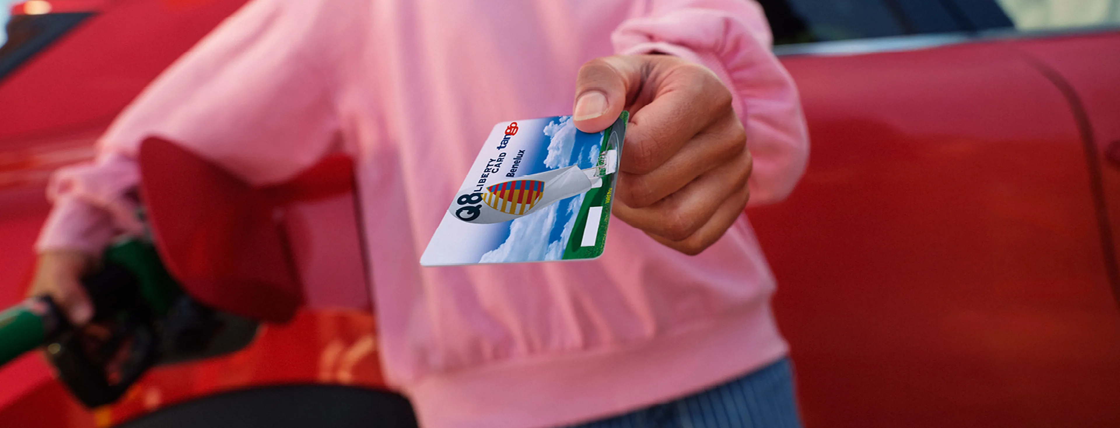 Une main tient une carte de carburant Q8 Liberty avec des voitures en arrière-plan