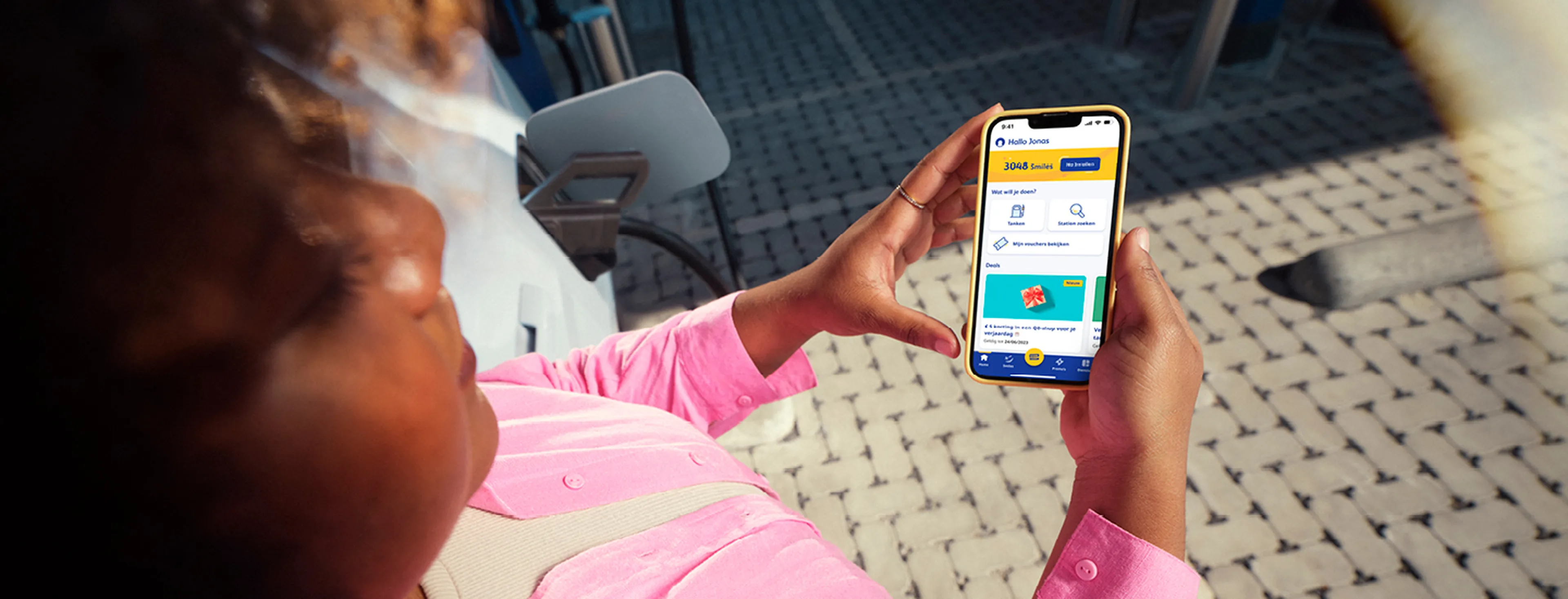 Une femme consulte l'application Q8 sur son téléphone dans une station-service Q8.