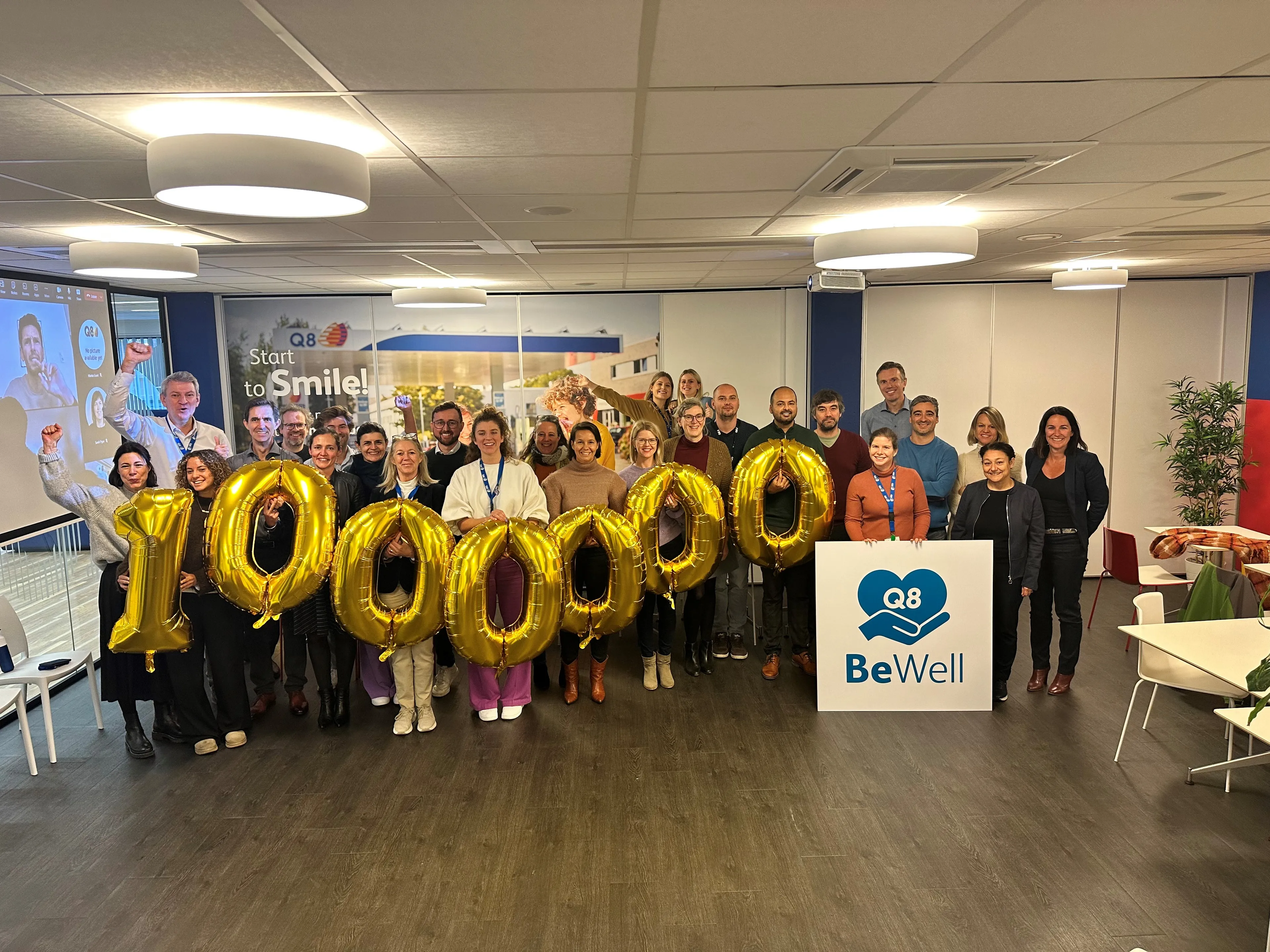 Un grand groupe de collègues tient des ballons numérotés et un panneau BeWell se trouve devant eux.