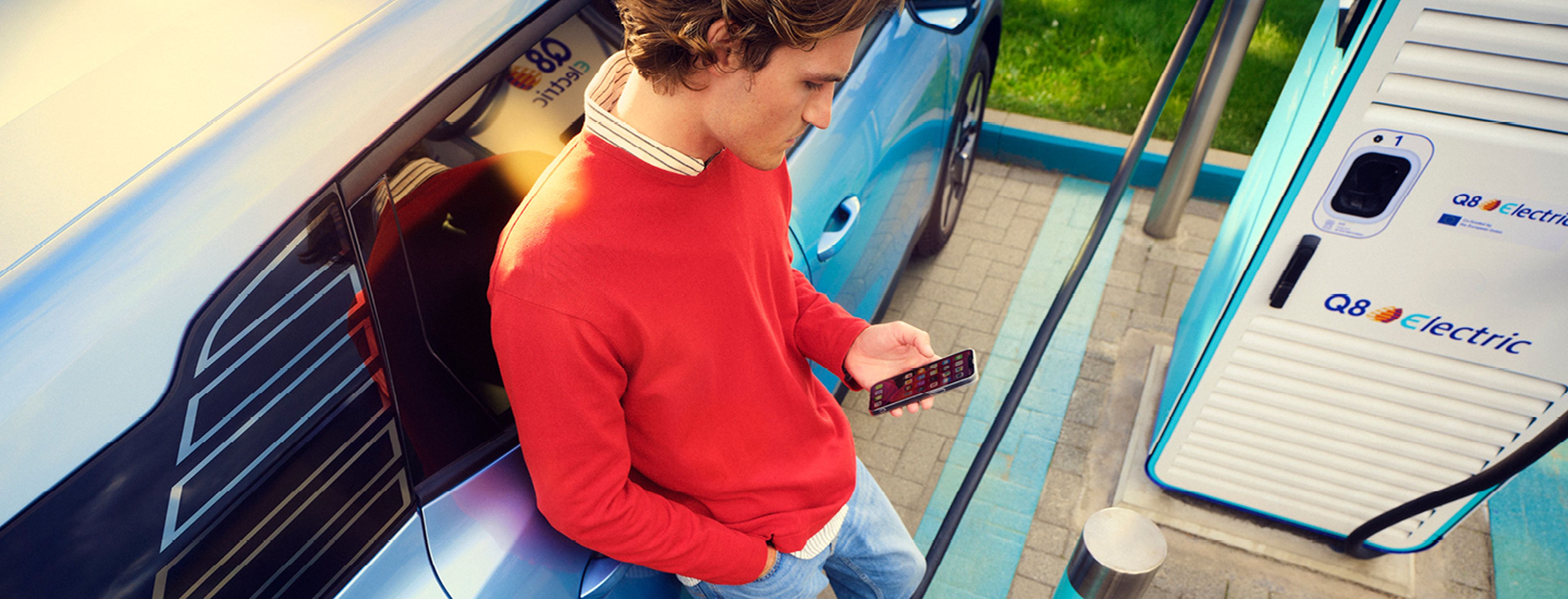 un homme a l'application électrique Q8 ouverte et charge à une station de recharge Q8