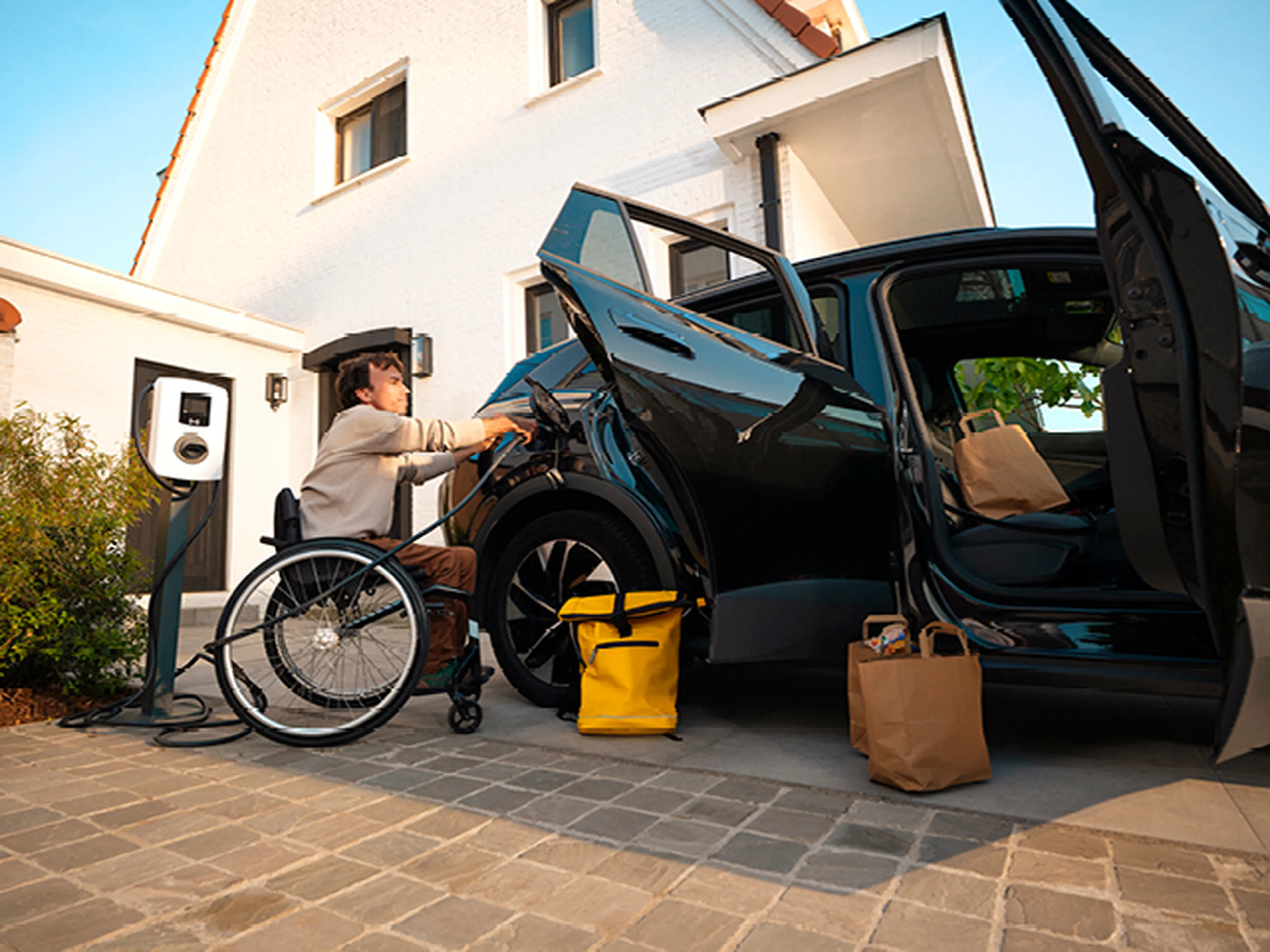 Homme en fauteuil roulant recharge une voiture électrique avec une borne de recharge domestique Q8