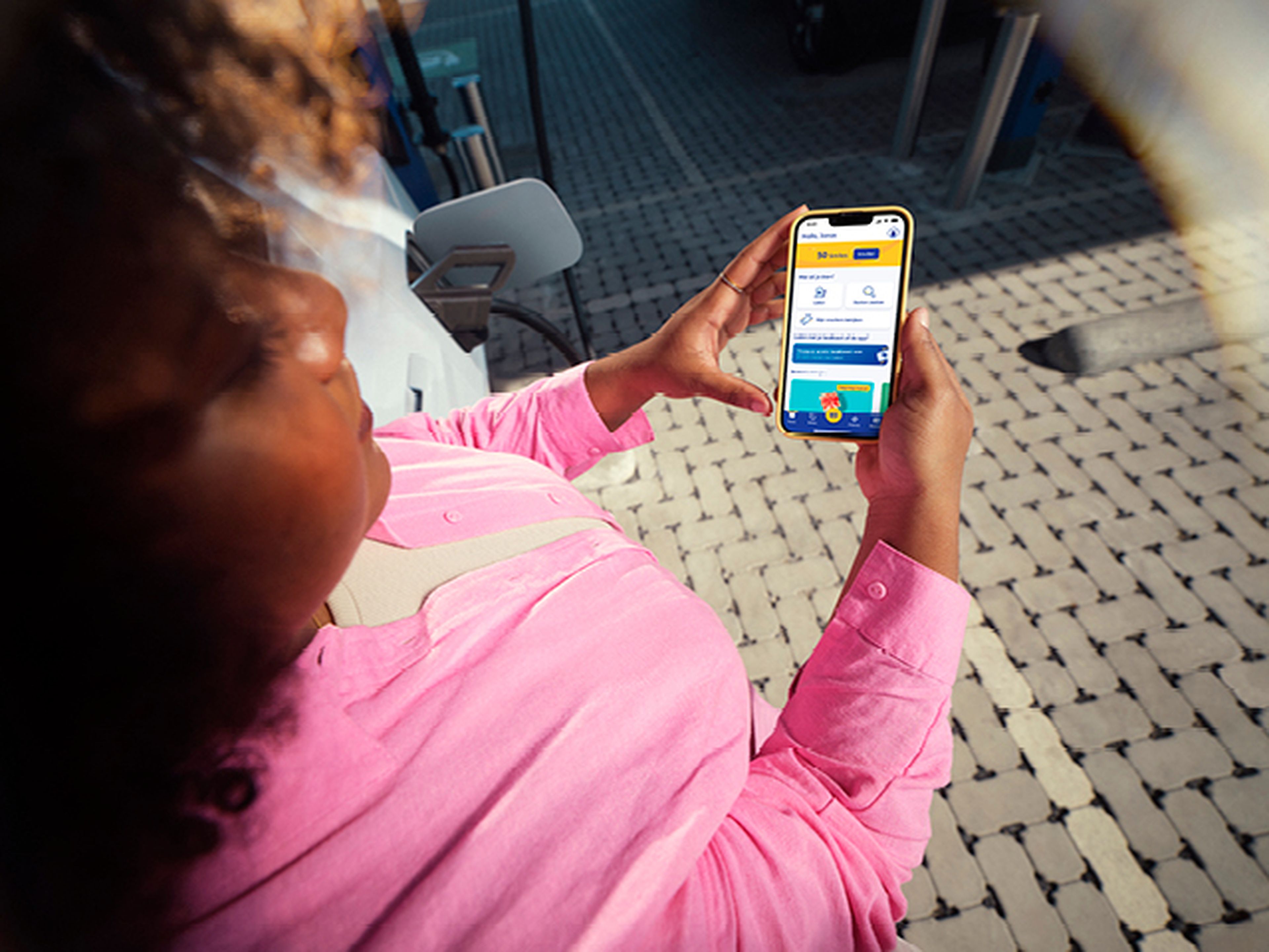 Femme regarde son téléphone à écran vert près d'une station de recharge Q8.
