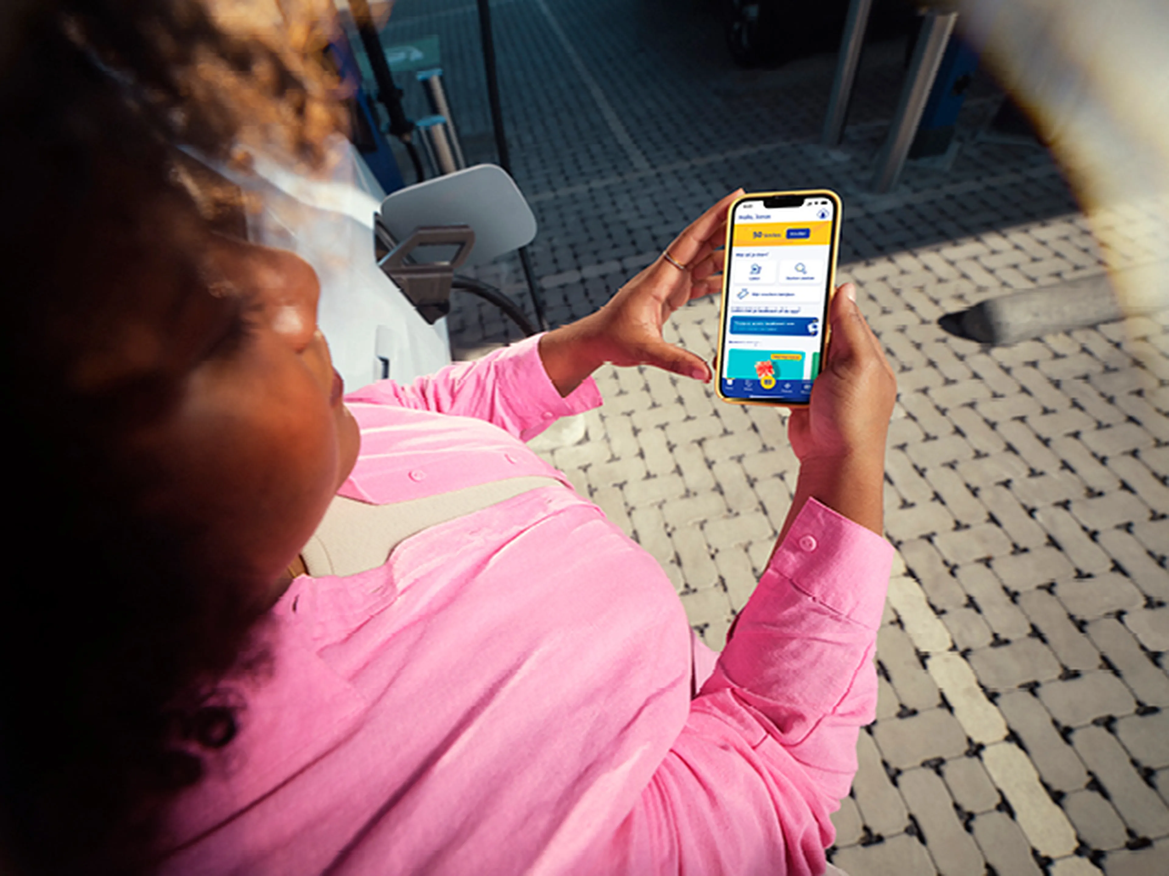 Femme regarde son téléphone à écran vert près d'une station de recharge Q8.​