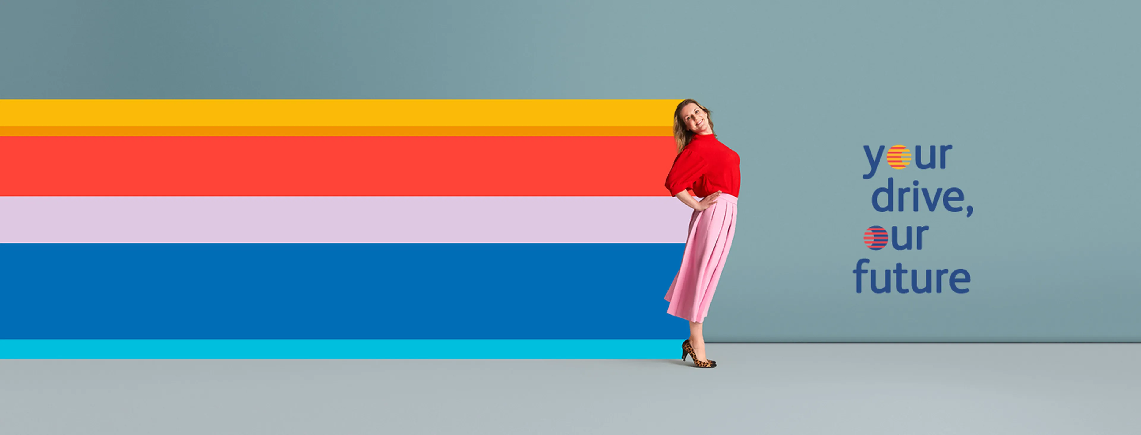 Une femme pose joyeusement en se penchant légèrement en arrière devant un fond bleu uni. Elle porte un haut rouge, une jupe plissée rose mi-mollet et des talons à imprimé léopard.