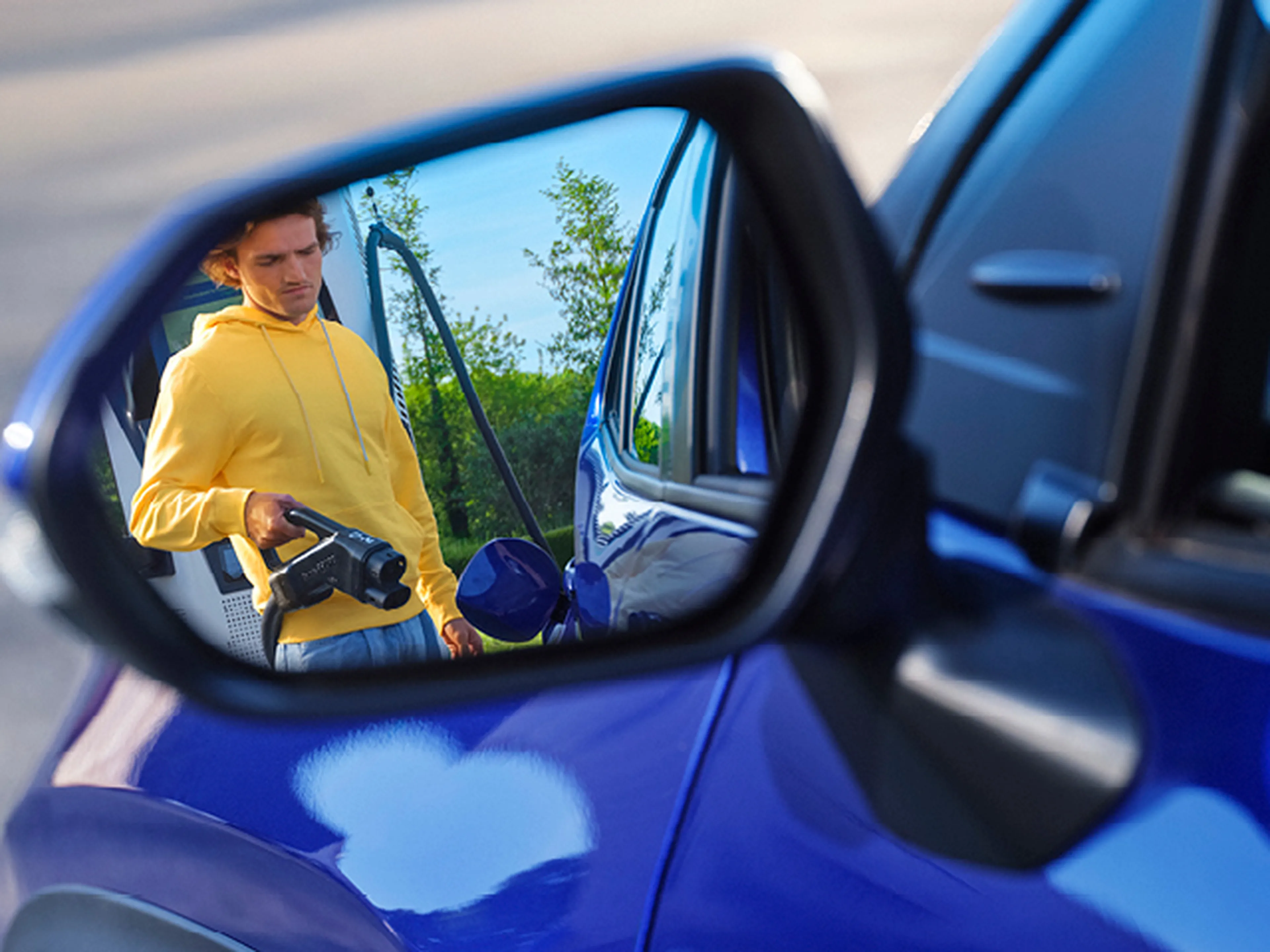 Homme avec câble de recharge se reflète dans le rétroviseur d'une voiture bleue chez Q8