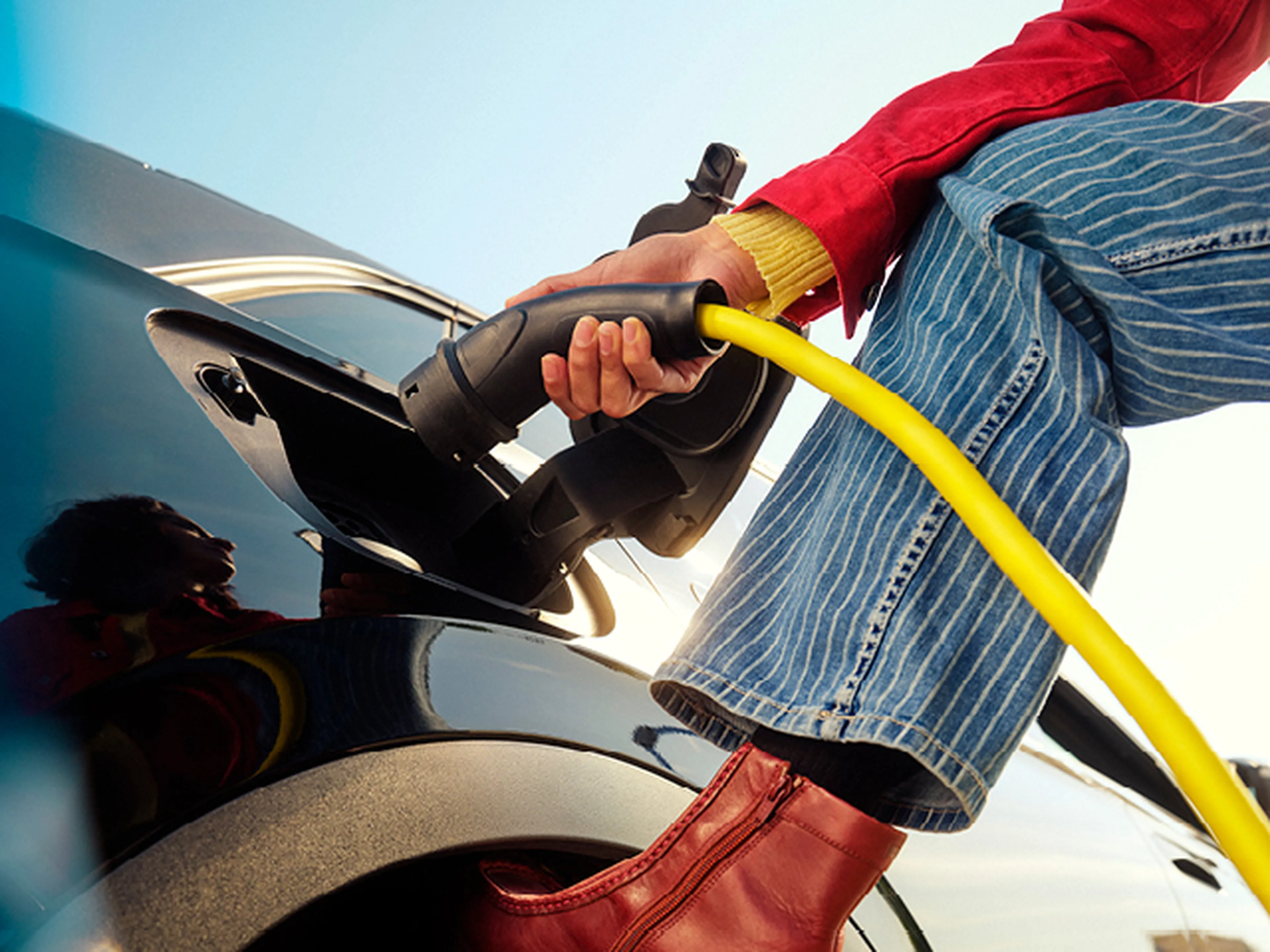 Femme recharge une voiture électrique avec un câble jaune chez Q8.