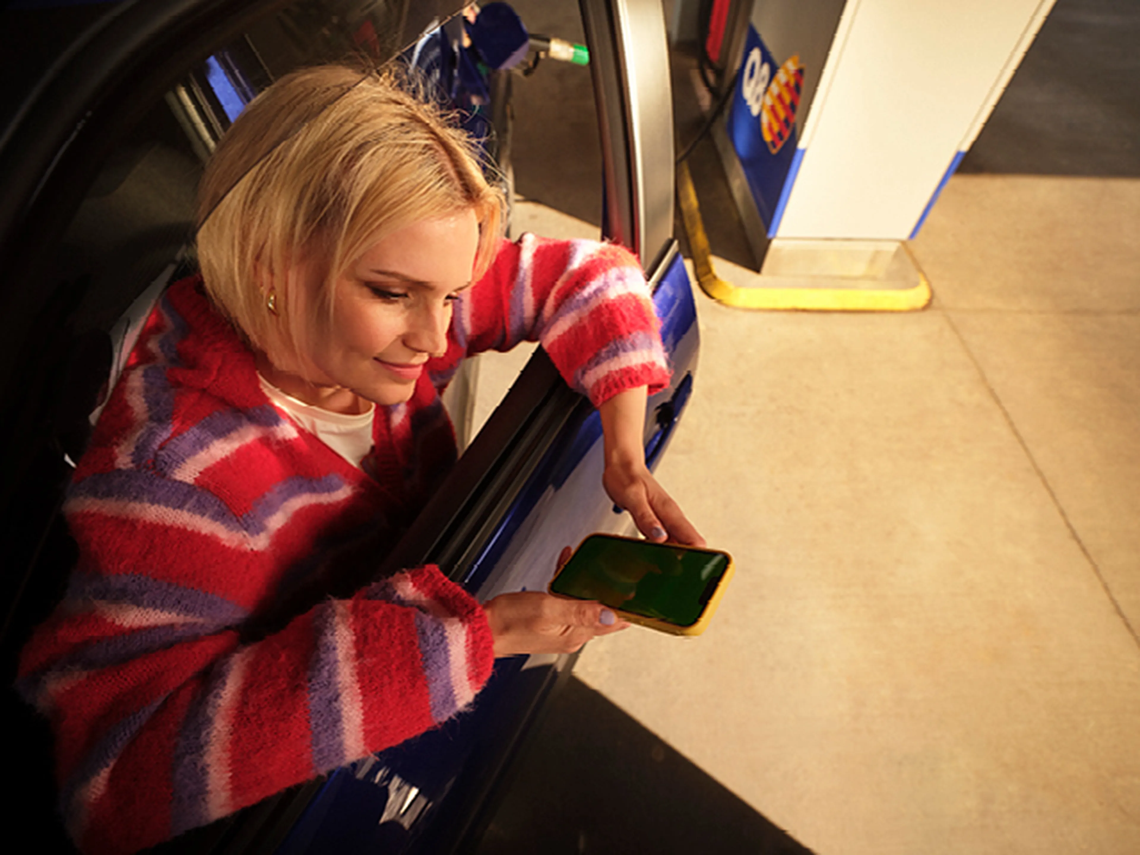 Femme regarde son téléphone depuis sa voiture chez Q8.​