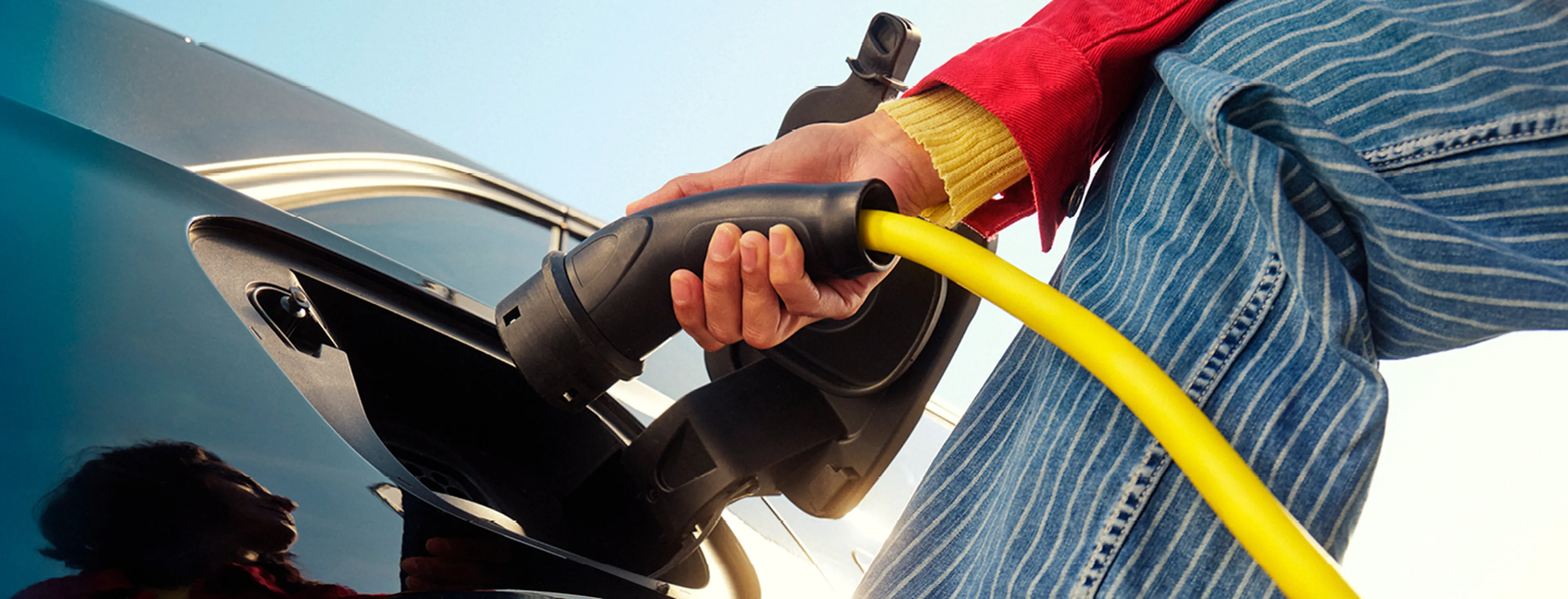 Femme recharge une voiture électrique avec un câble jaune chez Q8.