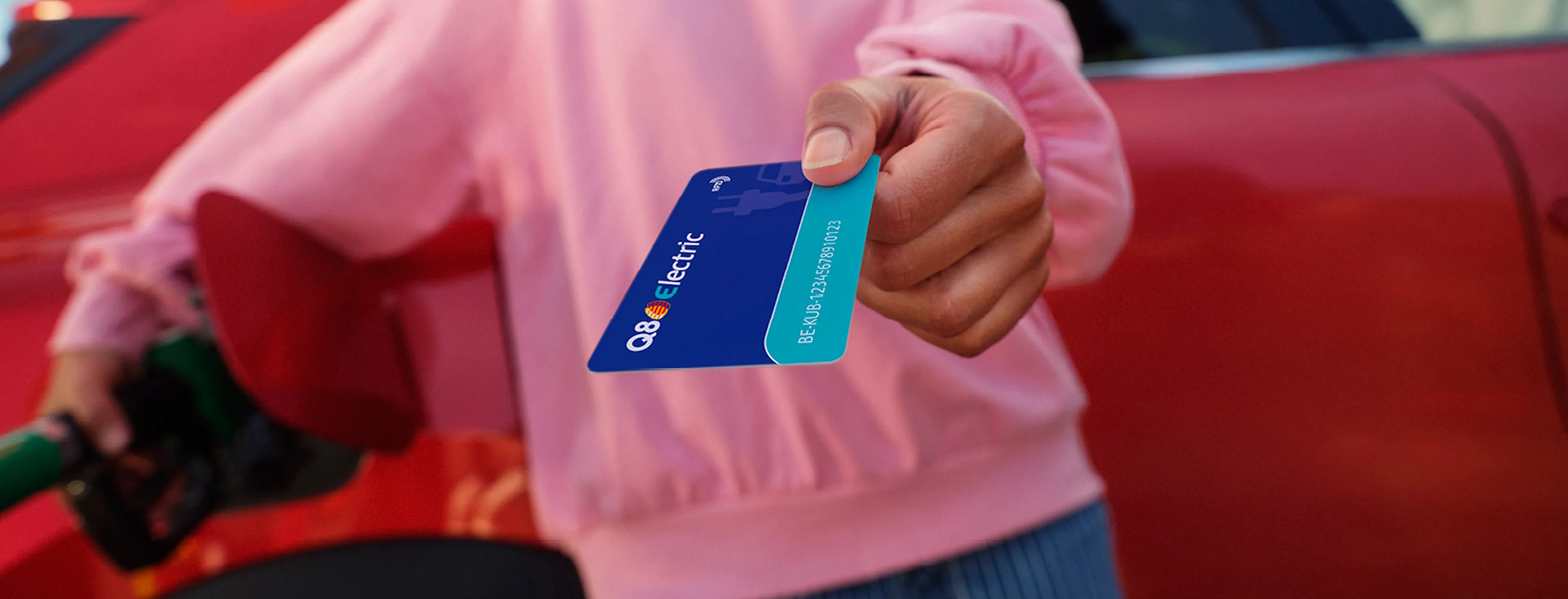 Femme montre une carte de recharge Q8 Electric près de sa voiture électrique chez Q8.
