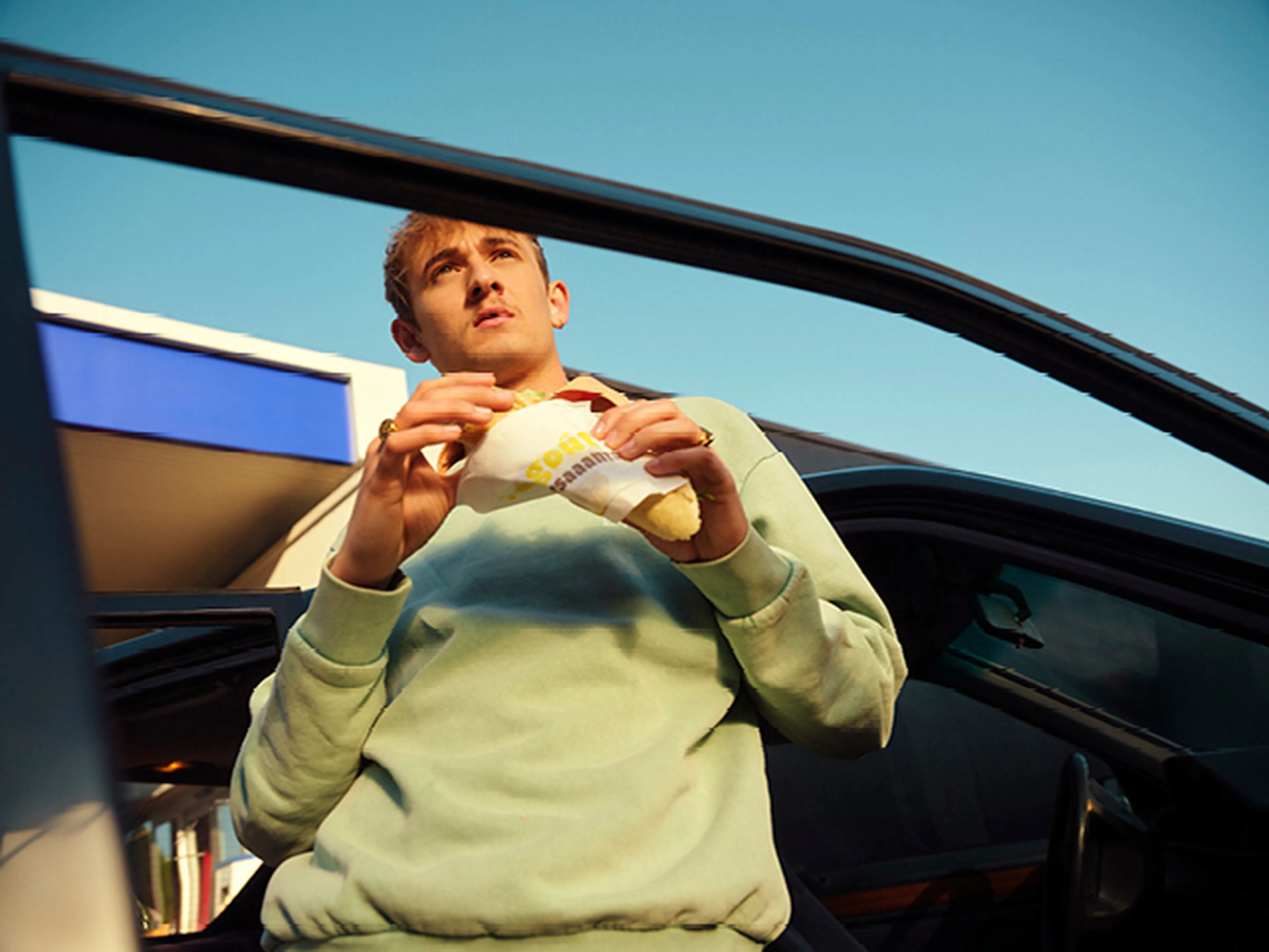 Homme debout près de sa voiture avec un sandwich Panos dans une station Q8