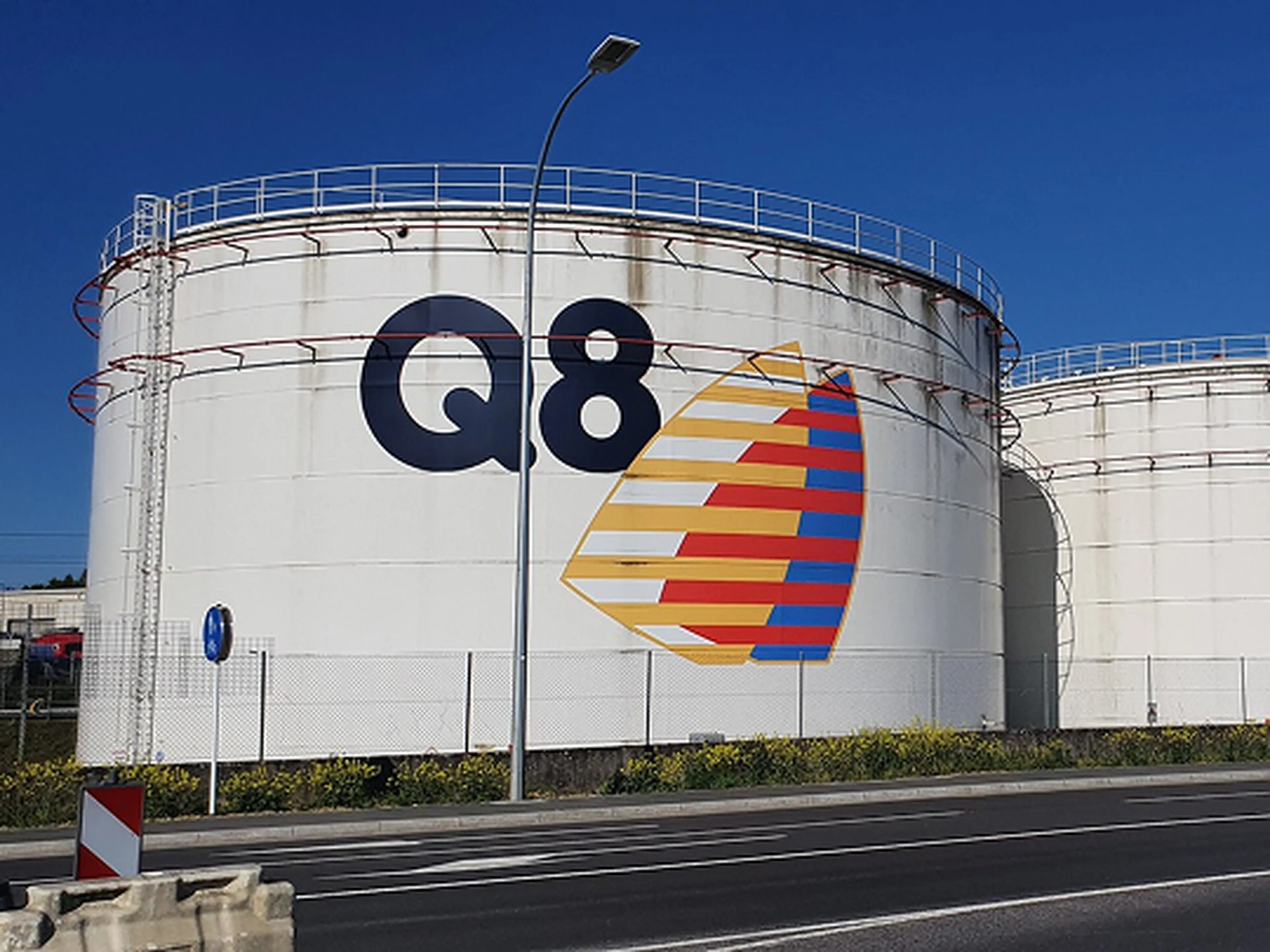Drie grote witte opslagtanks van Q8 langs een weg, met het Q8-logo op de linkertank.