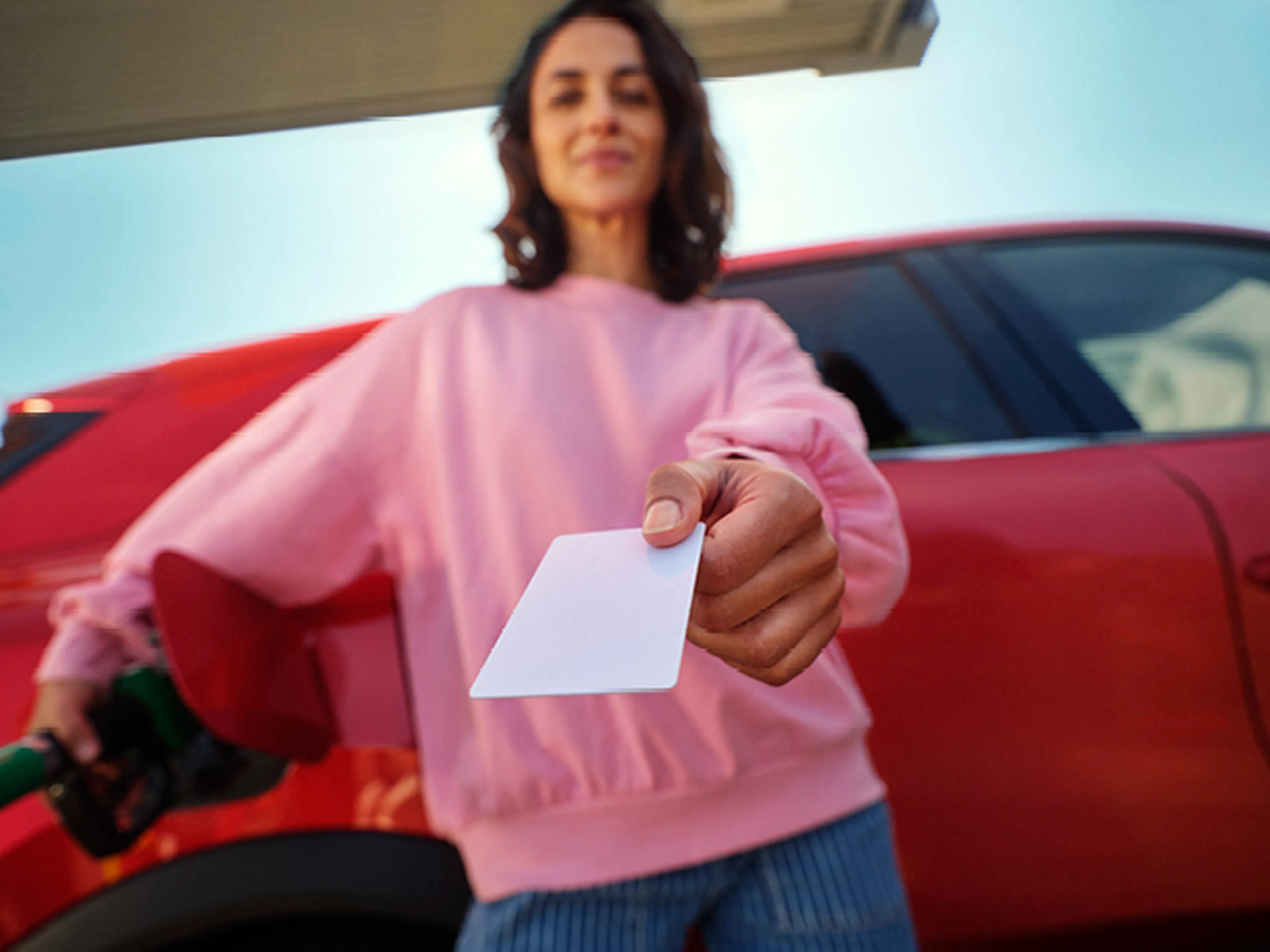 Femme montre une carte Q8 Liberty en faisant le plein d'une voiture rouge.