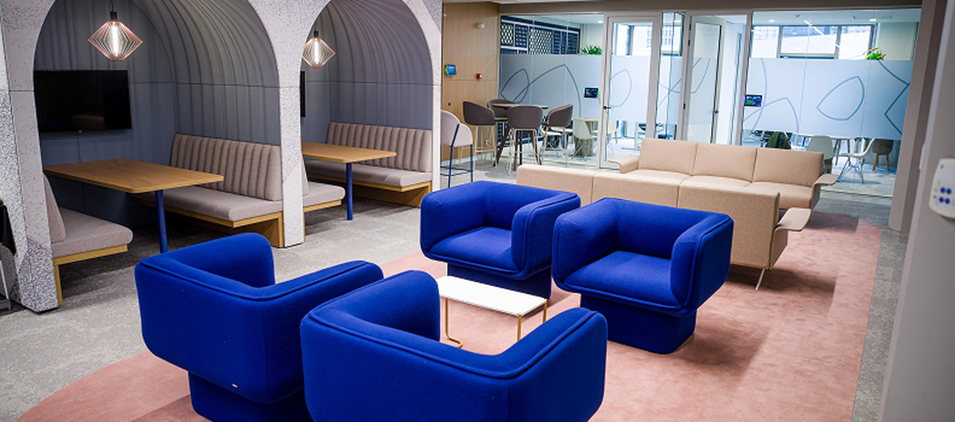 Espace lounge au siège de Q8 à Rotterdam avec des fauteuils bleu vif, des canapés beiges et des alcôves couvertes avec des tables.